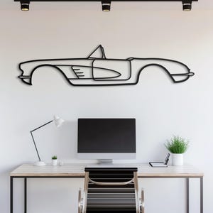 May include: A black line drawing of a classic convertible car on a white wall. The car is above a desk with a computer monitor, a lamp, and a plant.