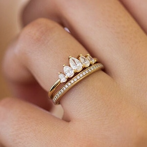 Op de afbeelding: Een gouden ring met een rij peervormige diamanten en een bijpassende band met kleinere diamanten.