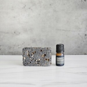 May include: A black lava rock diffuser with a small bottle of dark lavender essential oil. The bottle has a black label with the text "Farm Diffuser Dark Lavender Essential Oil 5ml".