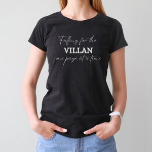 Puede incluir: Camiseta negra con el texto blanco "Falling for the VILLAN one page at a time". El texto está escrito en cursiva. La camiseta es de cuello redondo y está hecha de un material suave.
