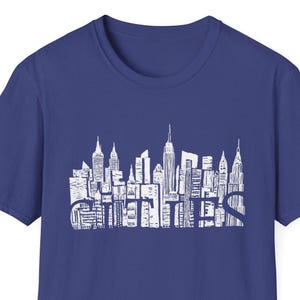 May include: A royal blue t-shirt with a white graphic of the New York City skyline. The graphic is made up of simple lines and shapes, creating a stylized representation of the city's iconic buildings.