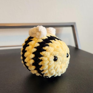 May include: A crocheted bee plush toy with black and yellow stripes, white fuzzy wings, and black button eyes.