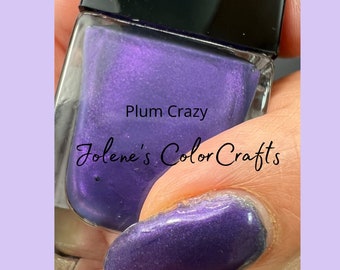Puede incluir: Una botella de esmalte de uñas morado con una etiqueta que dice "Plum Crazy" y "Jolene's Color Crafts". La botella está sobre un dedo con esmalte de uñas morado. El texto "Over Midnight Sky as base" está debajo de la botella.