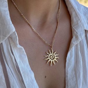 Pode incluir: Um colar de corrente de ouro com um pingente de sol. O pingente de sol tem um design em espiral.