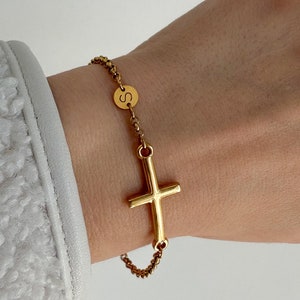 Peut inclure: Un bracelet en chaîne dorée avec un petit pendentif en forme de croix dorée et un pendentif rond en or gravé de la lettre "S".