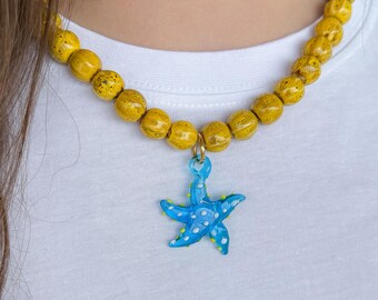 May include: A yellow wooden bead necklace with a blue starfish charm. The necklace is worn by a person with long brown hair.