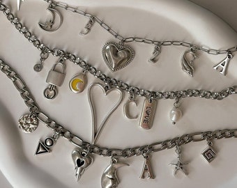 May include: A set of five silver chains with various charms, including hearts, moons, stars, letters, and a padlock. The charms are attached to the chains with small rings.