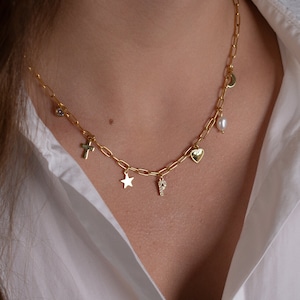 May include: A gold chain necklace with multiple charms, including a cross, a star, a letter 'P', a heart, a pearl, and a crescent moon.