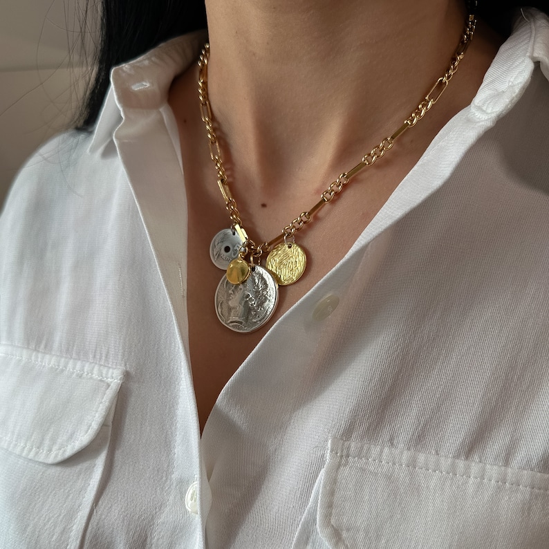Puede incluir: Un collar de cadena dorada con m&uacute;ltiples colgantes en forma de moneda. Los colgantes son una mezcla de plata y oro, y algunos tienen una superficie texturizada.