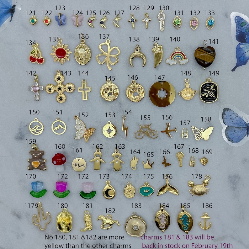 May include: A collection of 186 gold-tone charms, including a variety of shapes, symbols, and designs. The charms are arranged in rows on a white background. The charms are numbered from 121 to 186. The text "No 180, 181 &182 are more yellow than the other charms" and "Charms 181 & 183 will be back in stock on February 19th" is printed below the charms.