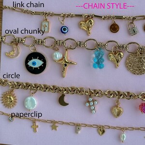 May include: Four gold chains with different link styles and charms. The top chain has a link chain style and charms including a cross, an evil eye, a heart, a smiley face, and a padlock. The second chain has an oval chunky link style and charms including a crescent moon, an evil eye, a pearl, a star, a gummy bear, a heart, and a circle. The third chain has a circle link style and charms including a sun, a pearl, a crescent moon, a cross with pearls, a heart, and a pink flower. The fourth chain has a paperclip link style and charms including a cross, a star, a letter P, a heart, and a pearl.