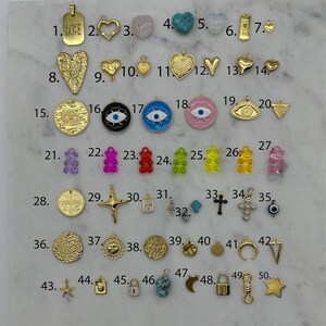 May include: Assortment of 50 gold-tone charms, including hearts, stars, crosses, a sun, a moon, a lock, a key, a bear, an evil eye, and a charm with the word "LOVE HOPE" on it.
