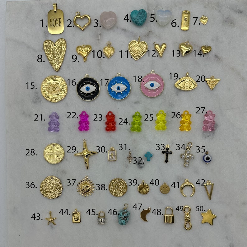 May include: Assortment of 50 gold-tone charms, including hearts, stars, crosses, a sun, a moon, a lock, a key, a bear, an evil eye, and a charm with the word "LOVE HOPE" on it.