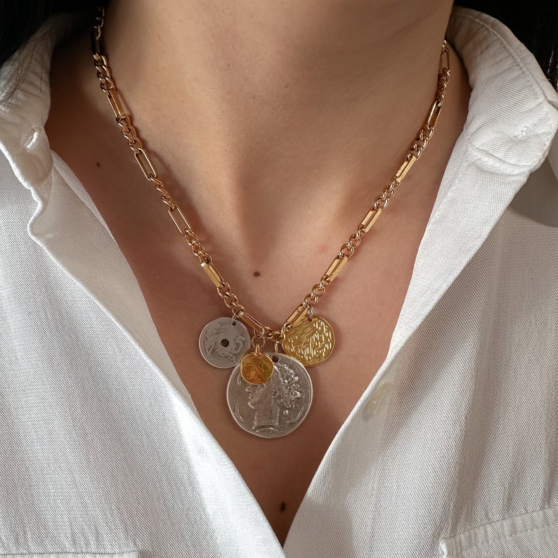 Puede incluir: Un collar de cadena dorada con varios colgantes de monedas. Las monedas son una mezcla de oro y plata y tienen diferentes dise&ntilde;os.
