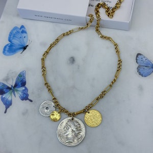 Puede incluir: Collar de cadena dorada con tres dijes de monedas. Las monedas son de plata y oro con diferentes dise&ntilde;os. La cadena es de estilo cadena de caja.