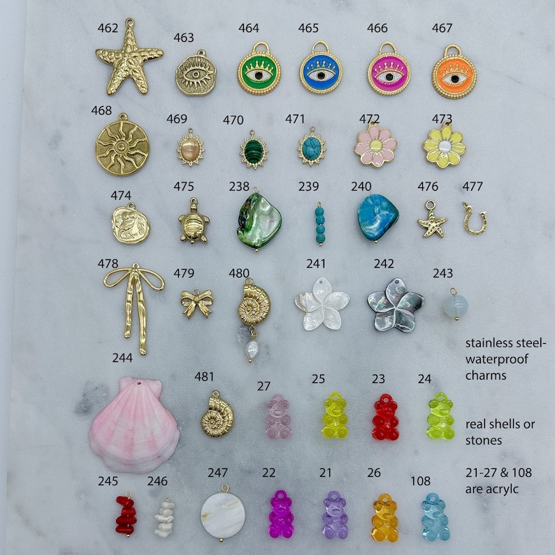 May include: An assortment of colourful charms and beads, including a starfish, seashells, a turtle, a crown, an eye, a flower, a horseshoe, a bow, a snail, a bear, and a gemstone. The charms are made of metal, acrylic, and natural materials. The text "stainless steel-waterproof charms" and "real shells or stones" is visible in the image. The text "21-27 & 108 are acrylic" is also visible in the image.