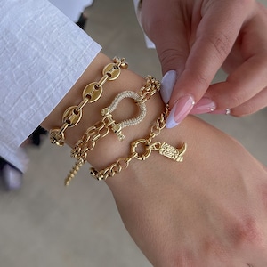 May include: Three gold bracelets with charms. The top bracelet is a chain with oval links. The middle bracelet has a horseshoe charm with clear rhinestones. The bottom bracelet has a boot charm.