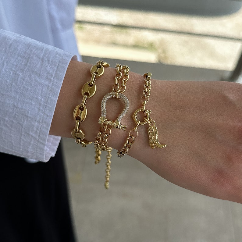 May include: A set of four gold bracelets featuring a horseshoe charm and a boot charm. The horseshoe charm is encrusted with clear stones.