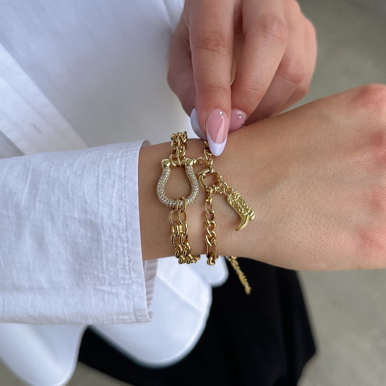 May include: A gold chain bracelet with a horseshoe charm and a boot charm. The charms are encrusted with clear rhinestones.