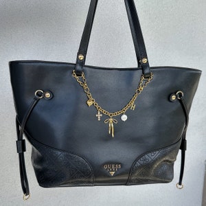 May include: Black leather tote bag with a gold chain and charms. The bag features a Guess Luxe logo on the front.