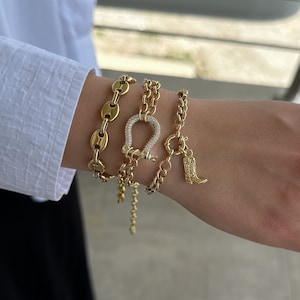May include: A set of four gold bracelets featuring a horseshoe charm and a boot charm. The horseshoe charm is encrusted with clear stones.