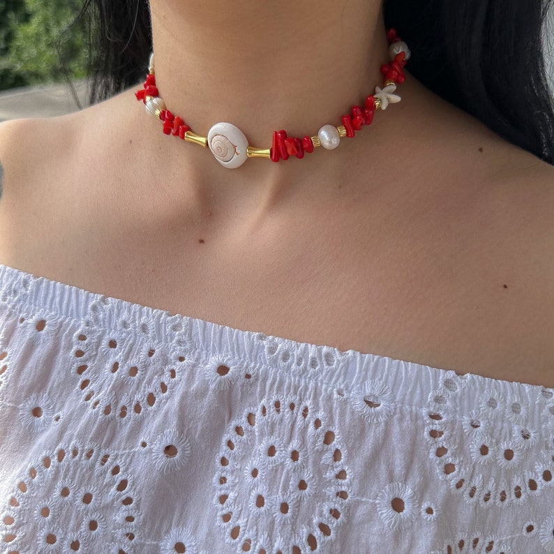 May include: A gold chain necklace with red coral beads, white pearls, and a white seashell pendant.