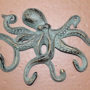 May include: A cast metal octopus wall hook with a distressed teal and gold finish. The octopus has eight curved arms with hook-shaped ends. The design is detailed with textured surfaces and is mounted on a neutral background.