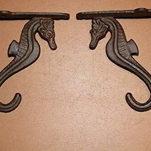 May include: Two cast iron seahorse shelf brackets. The brackets are dark brown with a seahorse design. The brackets are designed to be mounted on a wall to support a shelf. The seahorses are facing each other.