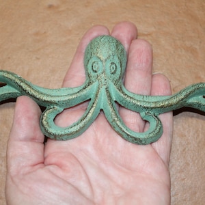 May include: A cast iron octopus-shaped wall hook with a distressed teal finish and gold accents. The octopus has eight curling tentacles and is designed for hanging items. The hook is a decorative nautical-themed item.