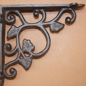 May include: A dark gray, cast iron shelf bracket with a decorative floral design. The bracket features stylized leaves and swirling patterns. The right angle design is suitable for supporting shelves. The bracket is made of metal.