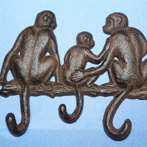 May include: A decorative cast iron wall hook featuring three monkeys sitting on a branch. The monkeys are brown with detailed textures, and their tails form the hooks. The piece is designed for hanging items.