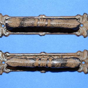 May include: Two matching drawer pulls featuring a textured, dark brown and tan finish. Each handle has an elongated, rectangular backplate with decorative, pointed ends and a central grip section with a ridged, horizontal design.