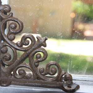 May include: Ornate, cast iron corner bracket with a dark brown, textured finish. The bracket features a decorative scroll design with a star-shaped element. It is designed to be mounted on a corner and adds a vintage touch.