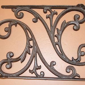 May include: Ornate, dark gray cast iron shelf brackets with a scrolling leaf and vine design. The brackets are rectangular with decorative flourishes and mounting holes, perfect for adding a vintage touch to any space.