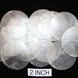 May include: A collection of translucent, round, mother-of-pearl shell discs, each approximately 2 inches in diameter, arranged against a black background. The iridescent surfaces reflect light, showcasing natural patterns.