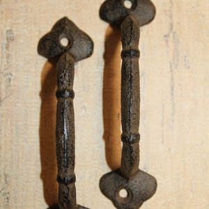 May include: Two dark gray, textured metal handles with a curved, segmented design. Each handle features a clover-shaped mounting plate at both ends, with a single circular screw hole centered in each plate for secure attachment to a surface.