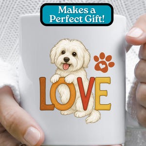 Puede incluir: Taza de caf&eacute; de cer&aacute;mica blanca con una imagen de dibujos animados de un perro blanco con la palabra "LOVE" en letras de colores. El perro sostiene una huella de pata con un coraz&oacute;n en el centro. El texto "Makes a Perfect Gift!" est&aacute; en un cuadro azul en la parte superior de la taza.