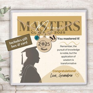 May include: A gold necklace with a compass charm and a 2025 charm. The necklace is in a white box with a gold background. The box also includes a graduation cap silhouette and the text "MASTERS CLASS OF 2025" and "You mastered it!" and "Congratulations! Love, Grandma".