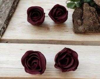 May include: Four burgundy felt roses, each with a different number of petals, are arranged on a wooden surface.