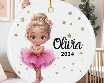 May include: A white ceramic ornament featuring a cartoon ballerina in a pink tutu, with the name "Olivia" and the year "2024" in black text. Gold stars and a gold string for hanging complete the design.