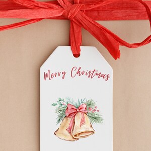 May include: A white gift tag with the text "Merry Christmas" in red cursive. The tag features a watercolor illustration of two gold bells with a red bow and green pine branches. The text "The Lorenzo Family" and "Elijah, Tiffany, Leo, and Skylar" is printed in brown at the bottom of the tag.