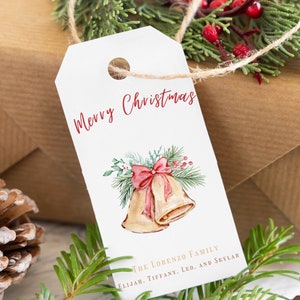 May include: White gift tag with red cursive text "Merry Christmas" and a watercolor illustration of two gold bells with a red bow and green pine branches. The text "The Lorenzo Family Elijah, Tiffany, Leo, and Skylar" is printed in gold at the bottom of the tag.