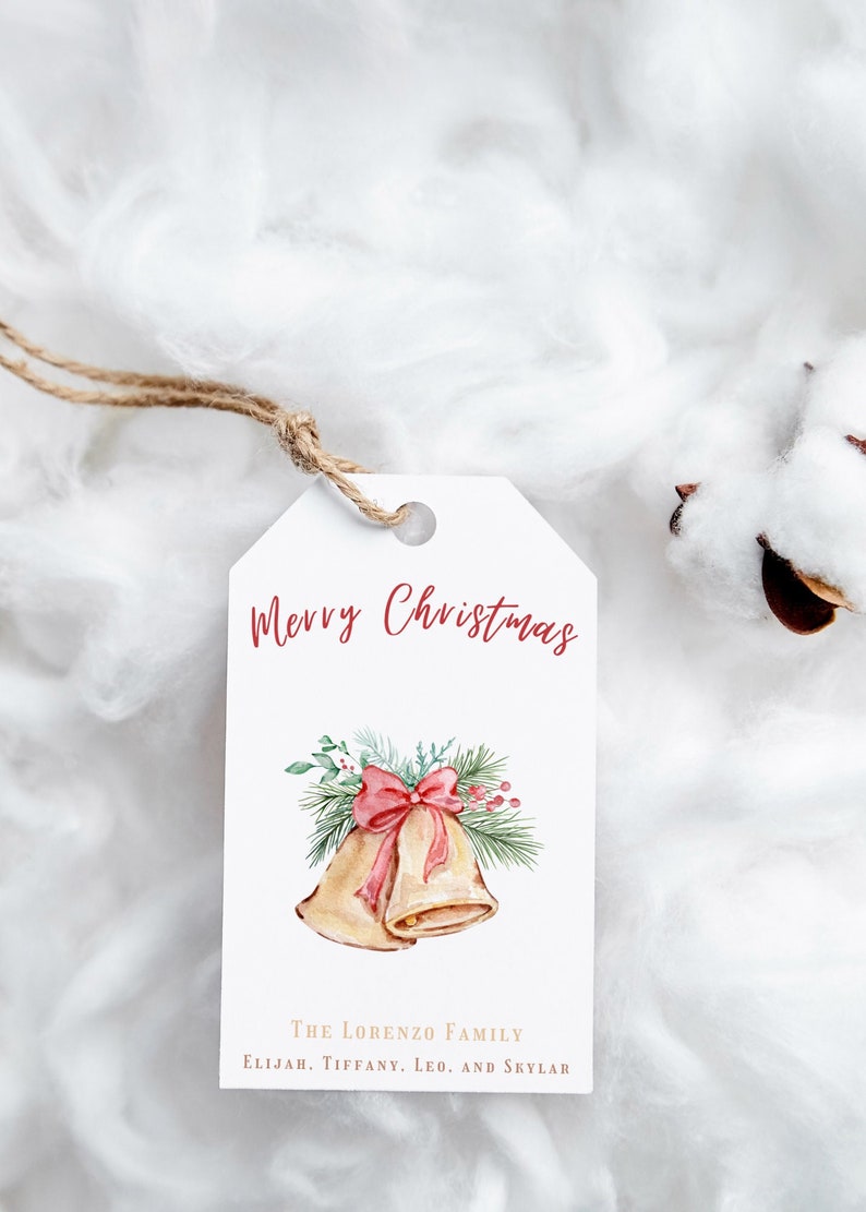 May include: A white gift tag with a watercolor illustration of two gold bells with a red bow and green pine branches. The text "Merry Christmas" is written in red cursive and the text "The Lorenzo Family Elijah, Tiffany, Leo, and Skylar" is written in brown.