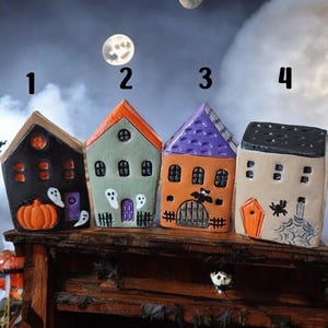 Peut inclure: Quatre maisons miniatures d'Halloween avec des designs et des couleurs différents. Les maisons sont en argile et peintes avec des détails comme des citrouilles, des fantômes, des chauves-souris et des araignées. Les maisons sont numérotées de 1 à 4.