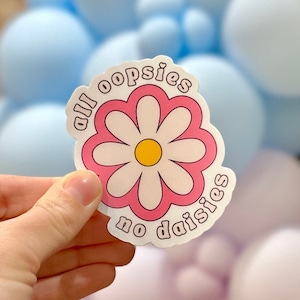 May include: A pink and white daisy sticker with the text "all oopsies no daisies" in a retro font.