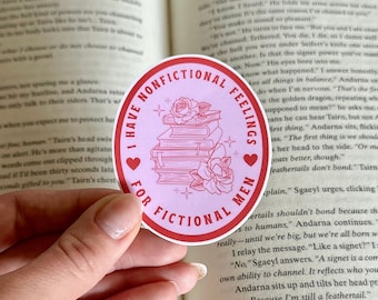 Könnte beinhalten: Ein runder Aufkleber in Pink und Rot mit dem Text "I Have Nonfictional Feelings For Fictional Men" in einem weißen Kreis mit einem Herzen auf jeder Seite. Der Aufkleber zeigt einen Stapel Bücher mit Blumen darauf.