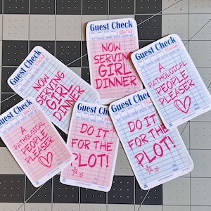 May include: Five pink and white guest checks with blue text. The checks have different phrases written on them, including "Now Serving Girl Dinner", "A Pathological People Pleaser", and "Do It For The Plot!"