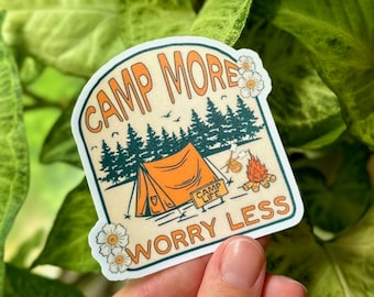 Könnte beinhalten: Ein Aufkleber mit einem Campingzelt, Bäumen und einem Lagerfeuer. Der Aufkleber lautet "Camp More Worry Less" mit einem kleineren Schild, auf dem "Camp Life" steht.