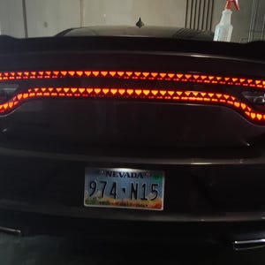 Può includere: Vista posteriore di un'auto grigio scuro con fanali posteriori rosso vivo. I fanali posteriori sono illuminati con un motivo di piccole luci individuali. È visibile una targa del Nevada. L'auto ha uno spoiler e doppi tubi di scarico.
