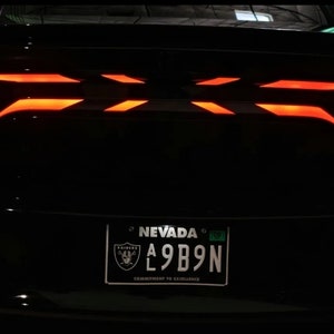 May include: Rear view of a black car with red taillights. The car has a Nevada license plate with the number A9B9N.